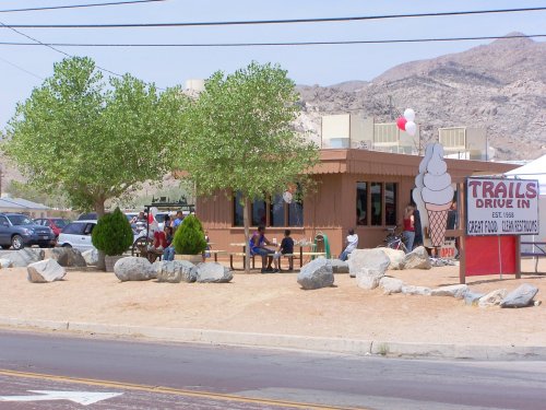 A drive-in ice cream shop with outdoor seating, surrounded by trees and rocks, in a desert landscape.