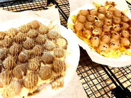 Two plates of dessert featuring round, doughy treats drizzled with caramel and sprinkled with powdered sugar.