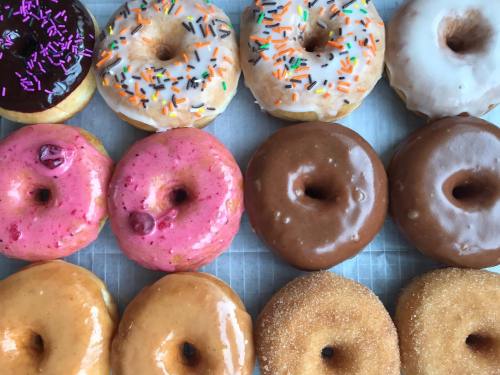 A variety of colorful donuts arranged in two rows, featuring sprinkles, glazes, and different flavors.