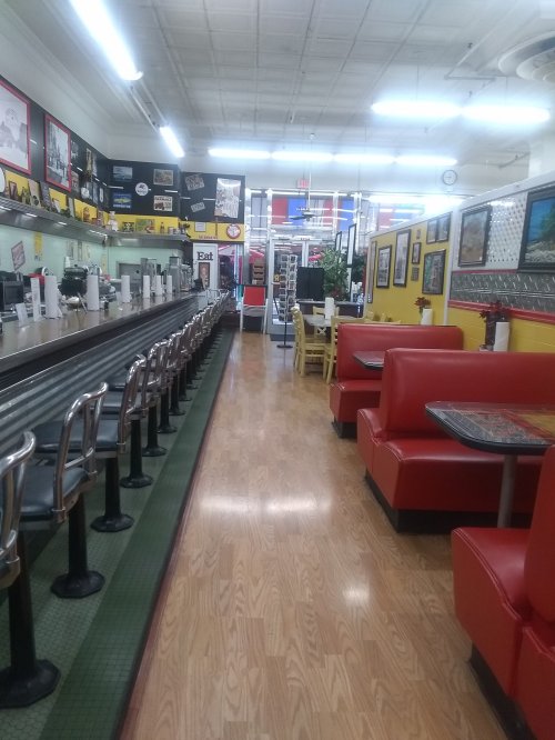 Interior of a diner featuring red booths, a long counter with stools, and colorful wall decor.