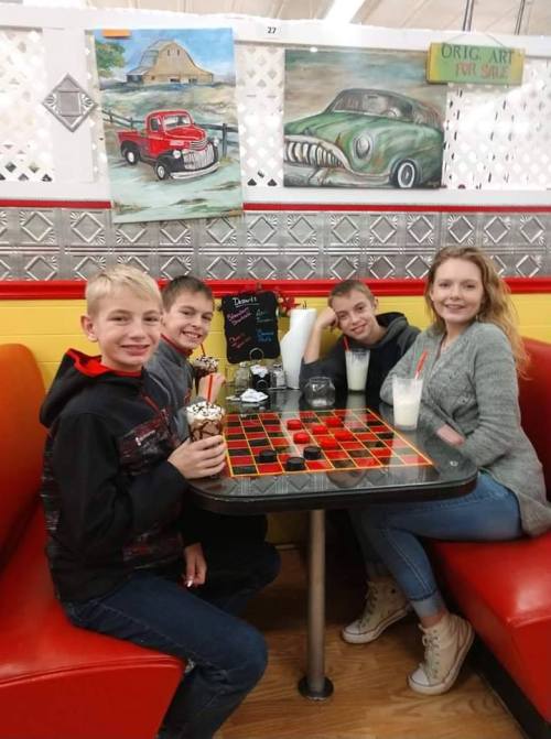 Four kids sitting at a diner booth, enjoying milkshakes and ice cream, with a colorful game board on the table.
