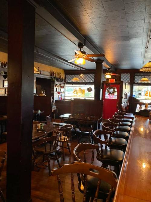 Interior of a cozy restaurant with wooden chairs, a bar, and warm lighting, featuring a welcoming atmosphere.