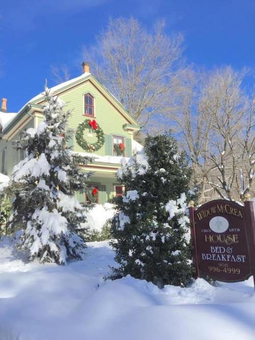 A charming green bed and breakfast covered in snow, with festive decorations and a sign in front.