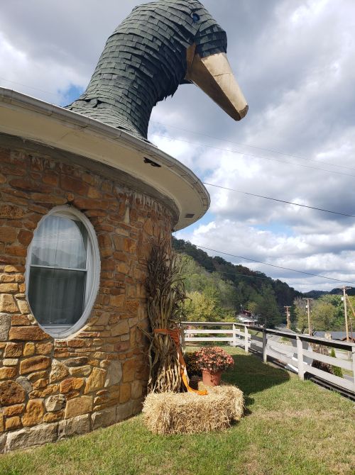A whimsical stone building with a large duck-shaped roof, decorated with hay bales and autumn plants.