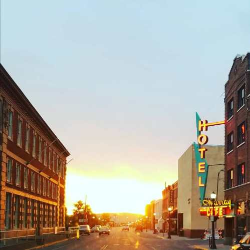 Sunset over a city street, featuring a hotel sign and vintage buildings on either side. Warm colors in the sky.