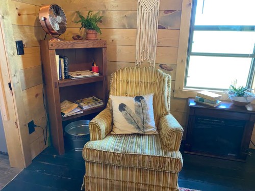 Cozy corner with a striped armchair, bookshelf, fan, and decorative plants in a wooden room.
