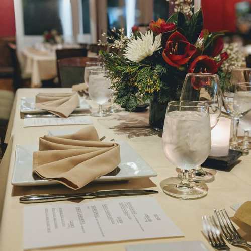 Elegant dining setup with neatly folded napkins, water glasses, and a floral centerpiece on a table.