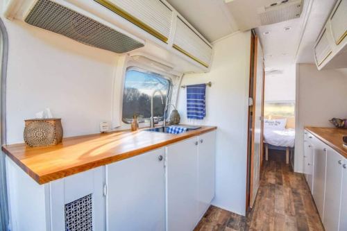 Interior of a modern camper van featuring a wooden countertop, sink, and a view into a cozy bedroom area.