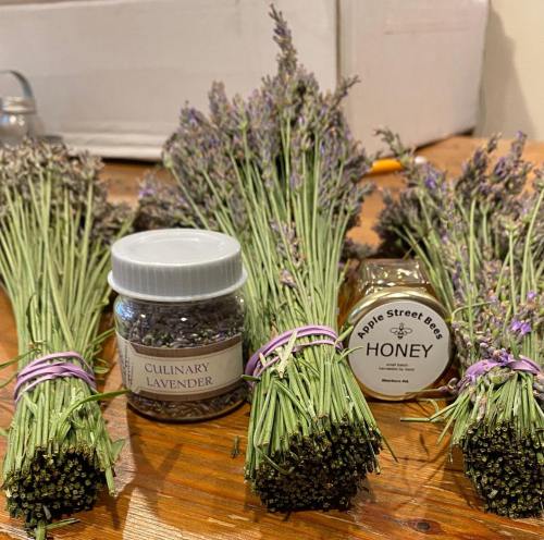 Bunches of dried lavender with a jar of culinary lavender and a jar of honey on a wooden table.
