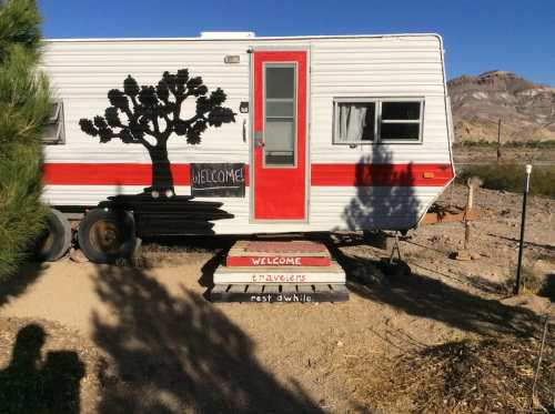 A vintage trailer with a tree silhouette, featuring a "Welcome" sign and steps inviting travelers to rest.