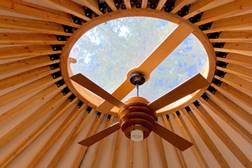 Ceiling view of a yurt featuring a circular skylight and a wooden ceiling fan.