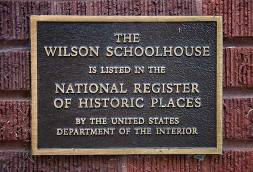 Plaque on a brick wall stating the Wilson Schoolhouse is listed on the National Register of Historic Places.