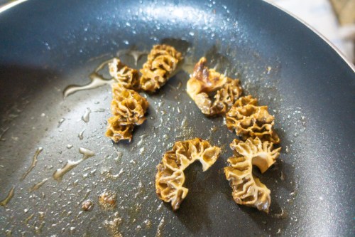Sautéed morel mushrooms in a frying pan with oil, showcasing their unique, curled shapes and rich brown color.