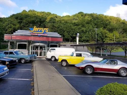 A retro diner named Jerry's Curb Service with classic cars parked outside, surrounded by greenery.