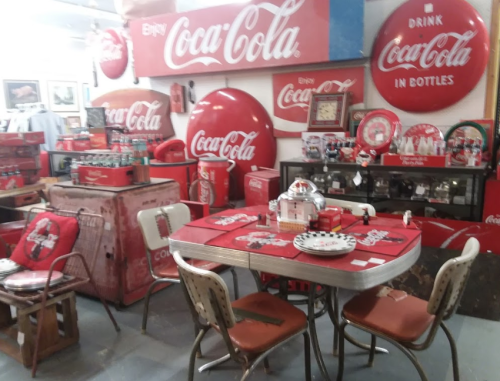 A vintage diner setup featuring Coca-Cola memorabilia, including a table, chairs, and decorative signs.