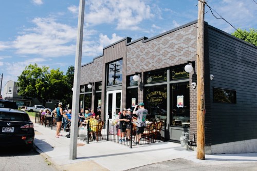 A busy ice cream shop with outdoor seating, people enjoying treats, and a clear blue sky in the background.
