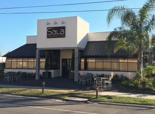 Exterior view of Sala Restaurant & Bar, featuring a modern design, outdoor seating, and palm trees.