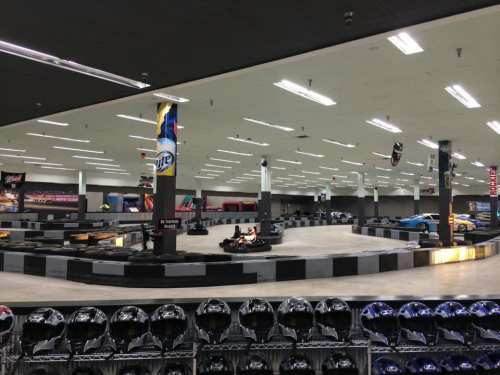 Indoor go-kart track with karts on the course and helmets displayed in the foreground. Brightly lit and spacious.