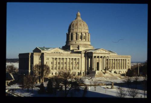 Historic building with a large dome, surrounded by snow-covered grounds and clear blue skies.