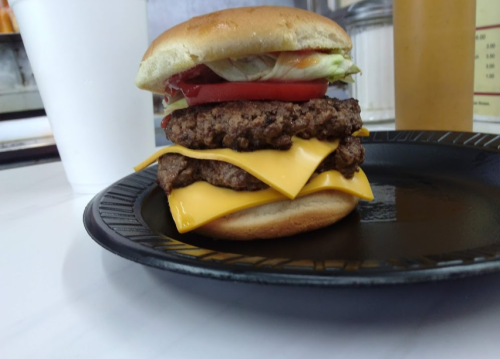 A stacked cheeseburger with two beef patties, melted cheese, lettuce, tomato, and ketchup on a bun, served on a black plate.
