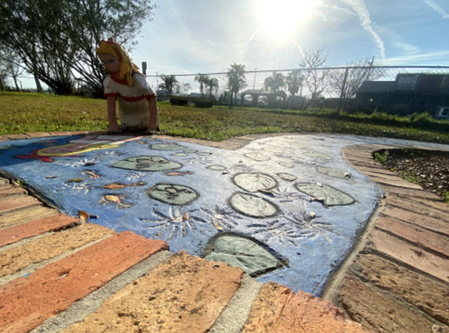 A colorful pathway with painted lily pads and a doll figure in a grassy area under a bright sky.