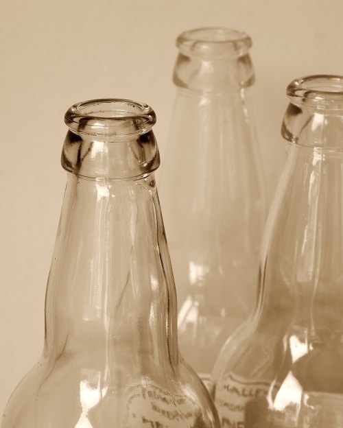 Three vintage glass bottles with narrow necks, set against a soft beige background.