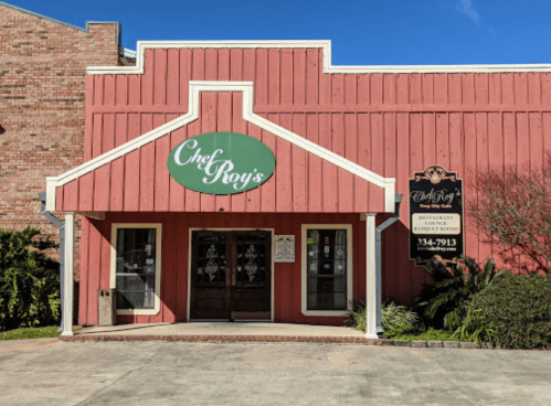 Exterior of Chef Roy's restaurant, featuring a red wooden facade and a green sign, under a clear blue sky.