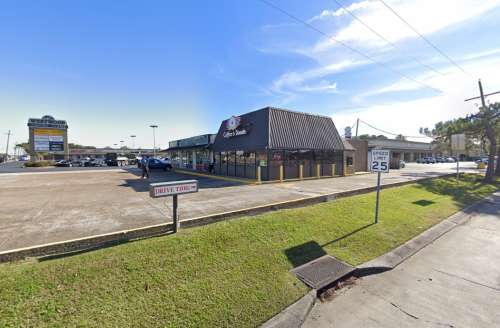 A fast-food restaurant with a drive-thru, surrounded by parking and a clear blue sky.