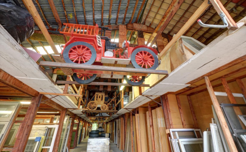 A vintage red toy truck suspended above a wooden structure filled with windows and other materials in a warehouse.