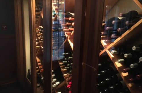 A wooden wine cellar filled with neatly arranged bottles on shelves, illuminated by soft lighting.