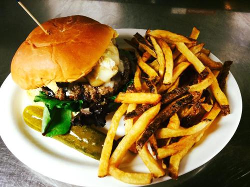 A juicy burger with melted cheese, lettuce, and a pickle, served with crispy golden fries on a white plate.