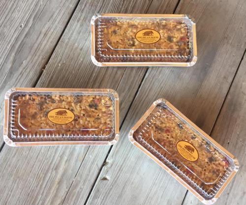 Three foil containers of pecan pie, each with a logo sticker, arranged on a wooden surface.