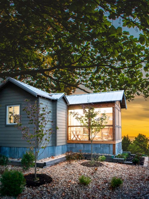 A modern house with large windows, surrounded by trees and a landscaped garden, at sunset.