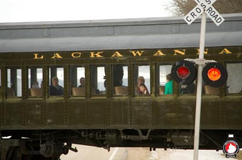 A vintage train labeled "Lackawanna" passes a crossing signal, with passengers visible in the windows.