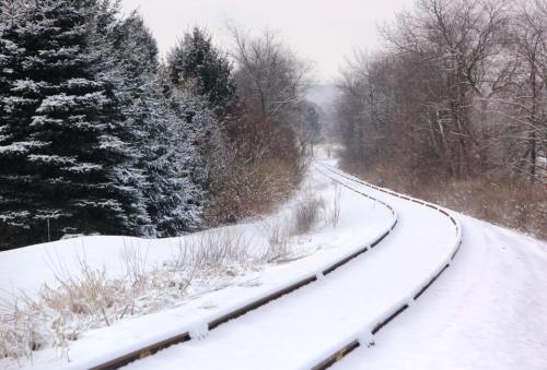 A snowy landscape featuring a winding railway track surrounded by trees and a blanket of snow.