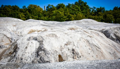 A landscape of white, sandy hills under a clear blue sky, surrounded by green trees in the background.