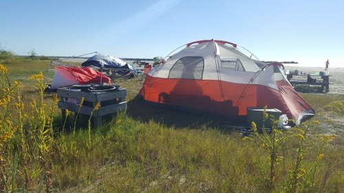 A colorful tent set up on grassy land near a beach, with other camping gear and a clear blue sky in the background.