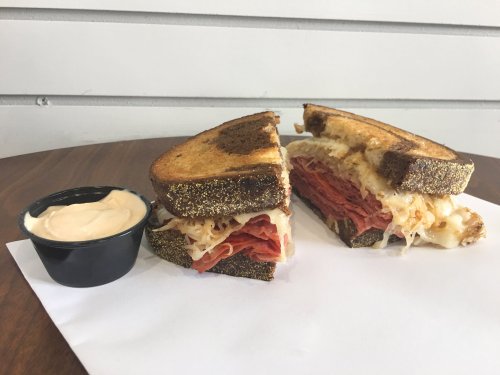 A sliced sandwich with layers of corned beef, sauerkraut, and melted cheese, served with a side of dipping sauce.