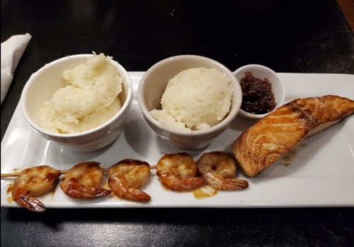 A plate with grilled salmon, shrimp skewers, mashed potatoes, and a small dish of sauce.