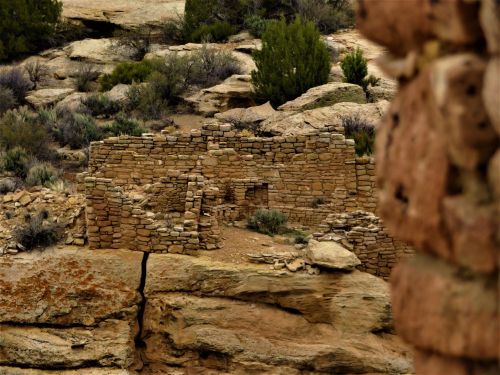 Ancient stone ruins nestled among rocky terrain and sparse vegetation in a desert landscape.