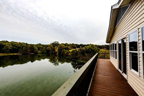 A serene view of a lake from a wooden deck, surrounded by trees under a cloudy sky.