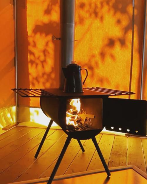 A cozy wood stove with a kettle on top, casting warm light and shadows against an orange backdrop.