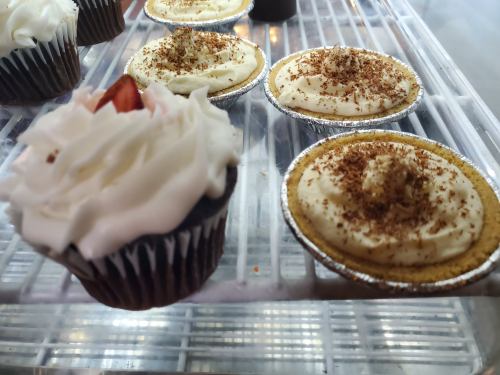 A close-up of a chocolate cupcake with white frosting next to mini cream pies topped with chocolate shavings.