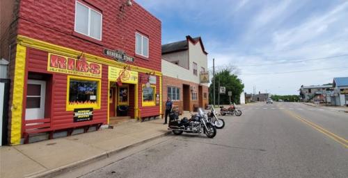 Colorful storefronts line a quiet street, with motorcycles parked outside a rib restaurant and general store.