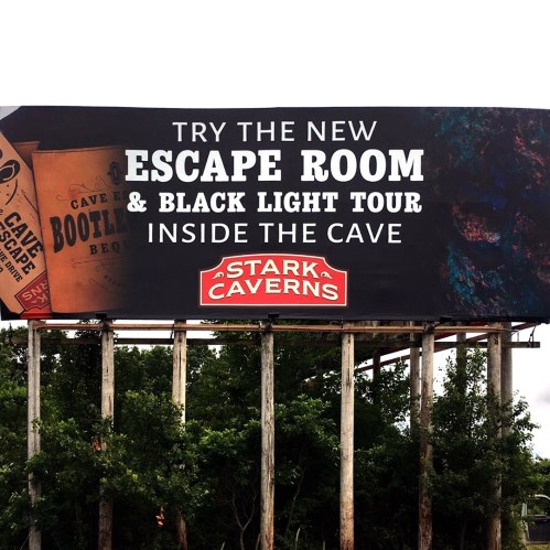 Billboard promoting a new escape room and black light tour at Stark Caverns, featuring cave-themed graphics.