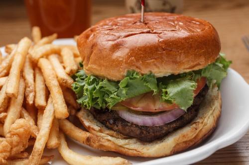 A juicy burger with lettuce, tomato, and onion, served with a side of crispy French fries on a white plate.