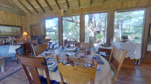 Cozy dining area with a wooden table set for a meal, surrounded by large windows and rustic decor.