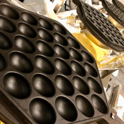 Close-up of a waffle maker with multiple round molds, ready for cooking.