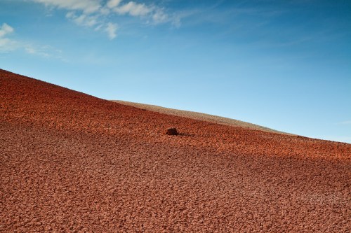 A vast landscape of textured red and gray hills under a clear blue sky.