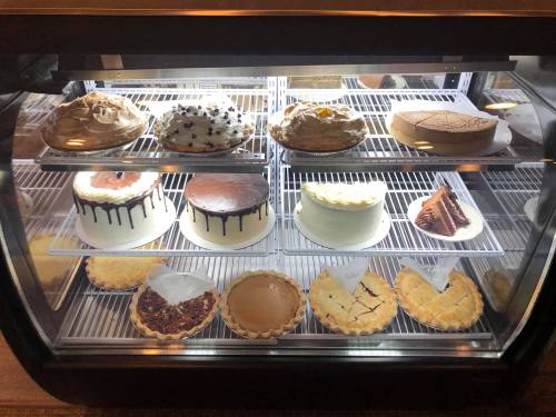 A display case filled with various cakes and pies, including chocolate, fruit, and cream desserts.